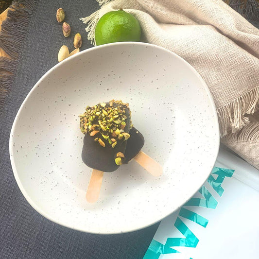 two chocolate and pistachio collagen ice blocks on a plate with collagen pack and lime in background