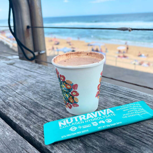 coffee on a bench at beach with a collagen sachet in front of it