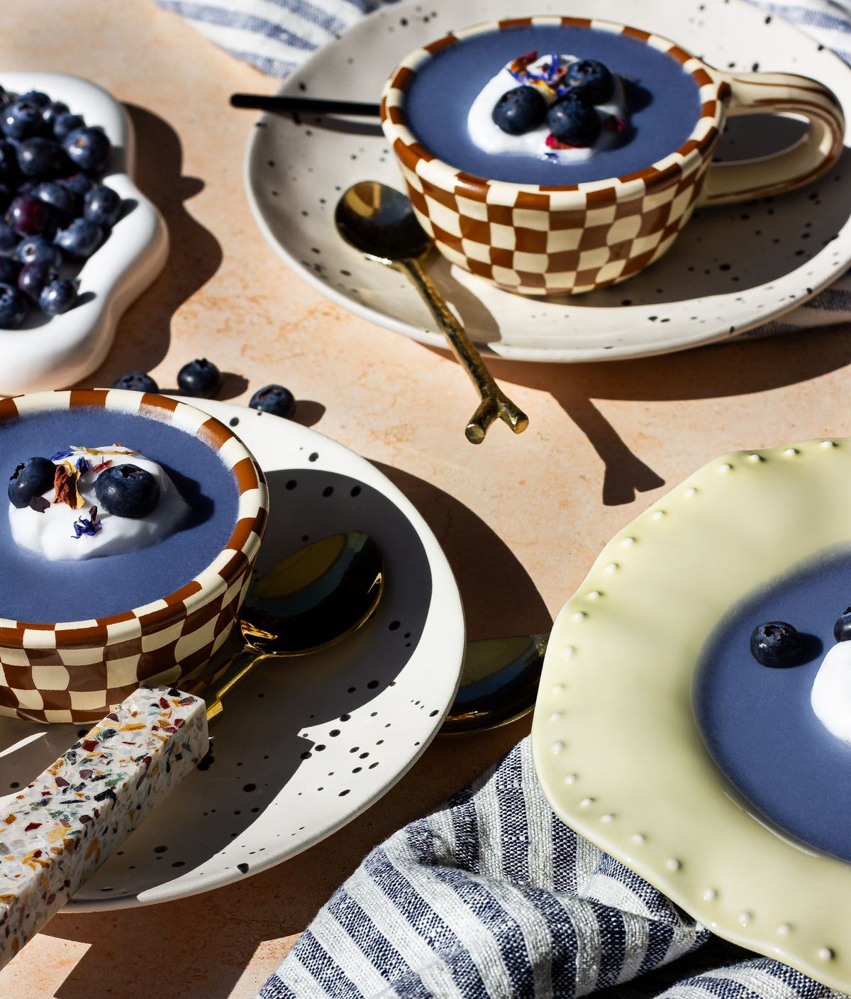 Three ceramic cups of a blended drink topped with yoghurt and blueberries on a sunlit bench